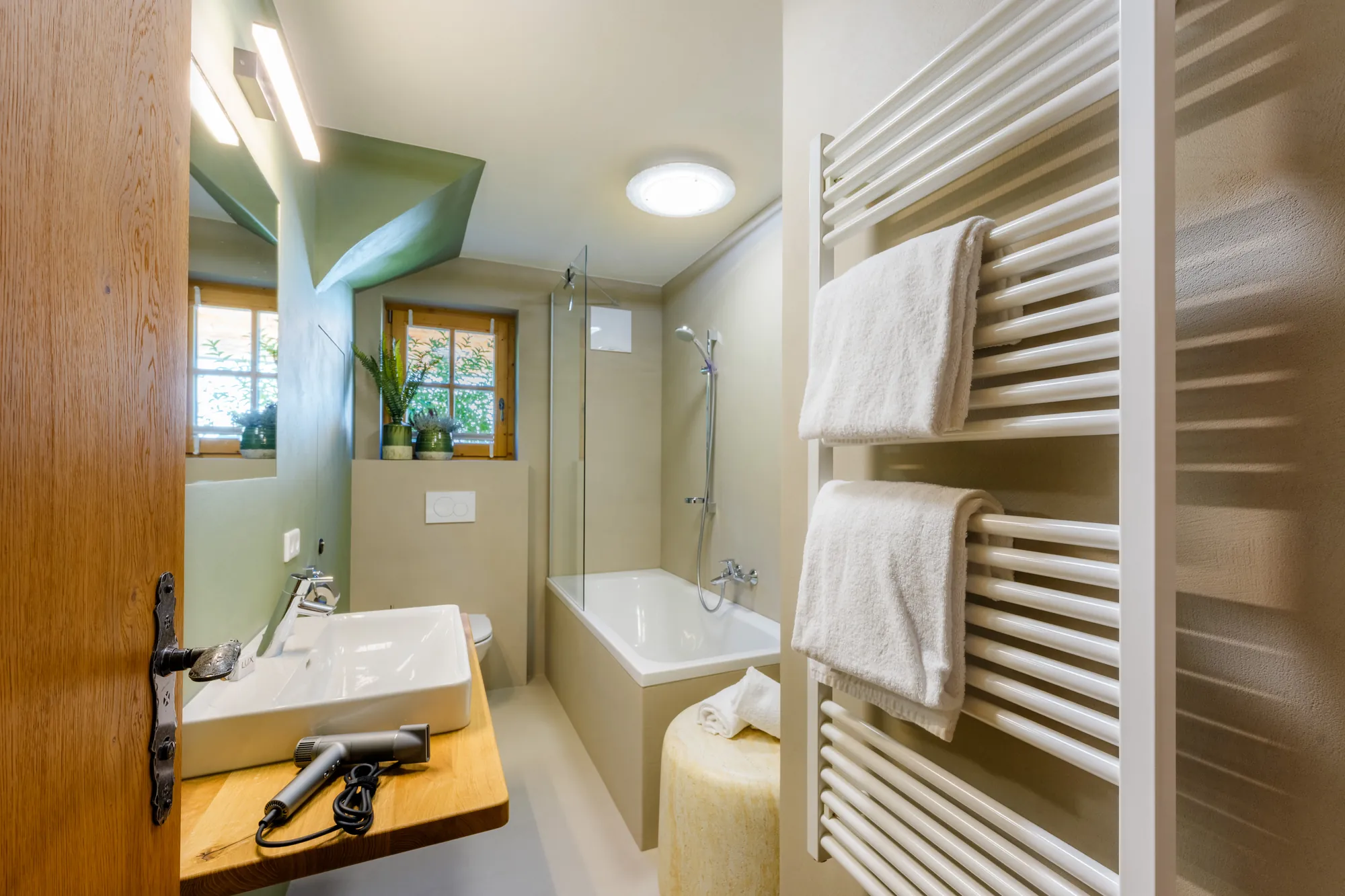 Bright bathroom with bathtub, washbasin on a wooden shelf, hairdryer and heated towel rail with white towels