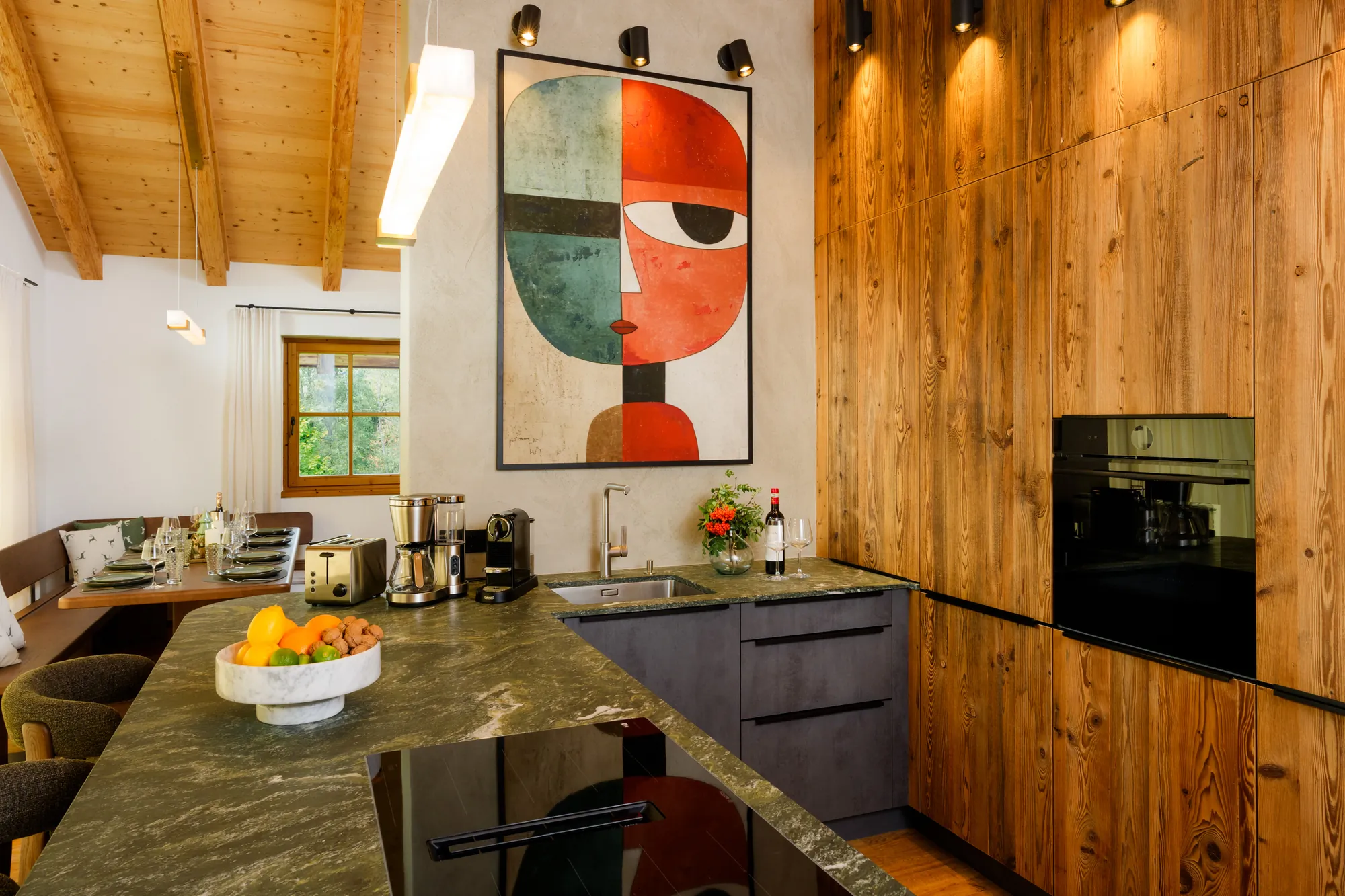 Designer kitchen with island, green stone worktop, wooden fronts, oven and a large artwork on the wall