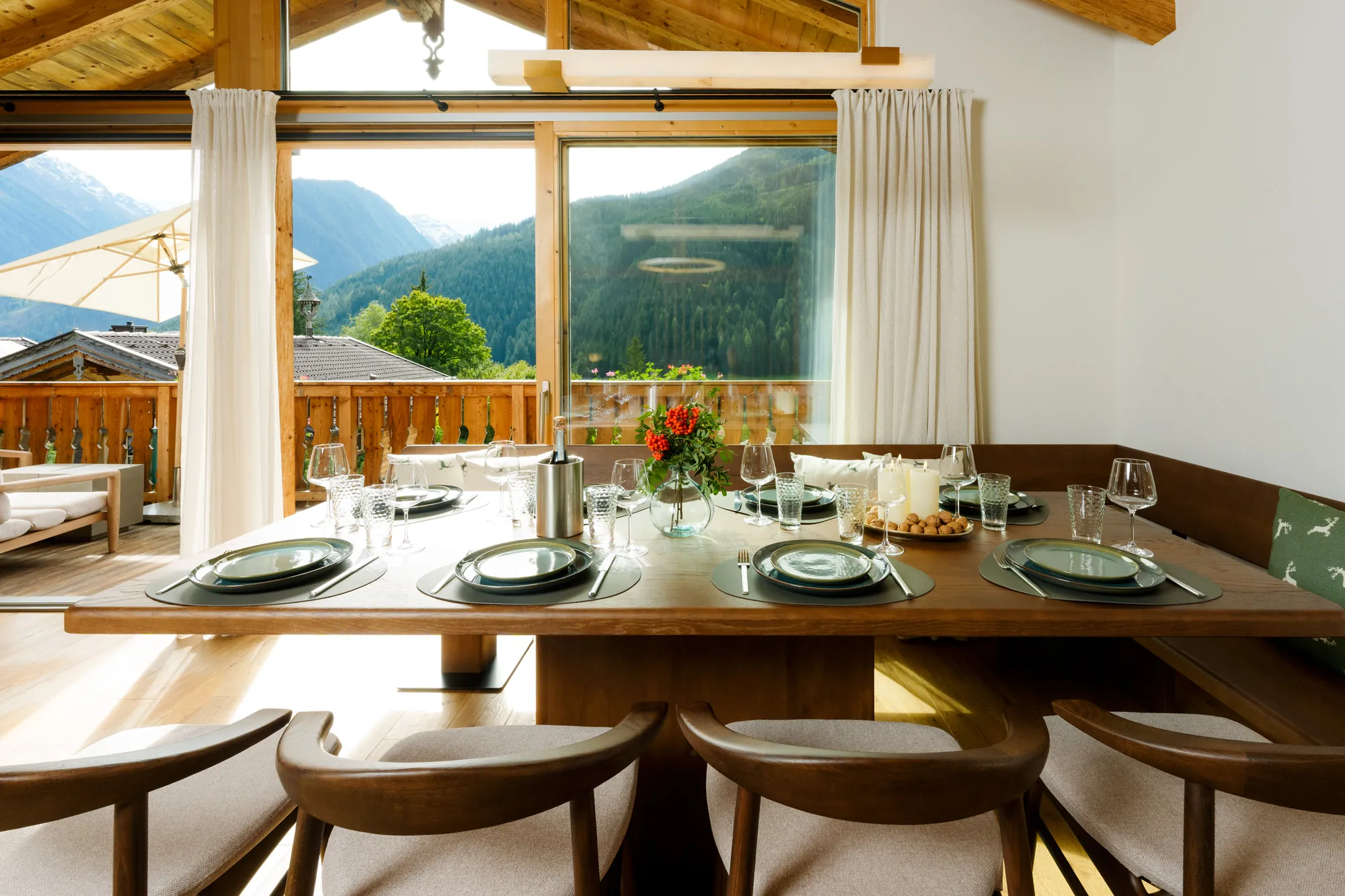 Set solid-wood dining table with corner bench and chairs in front of large windows overlooking balcony and mountains