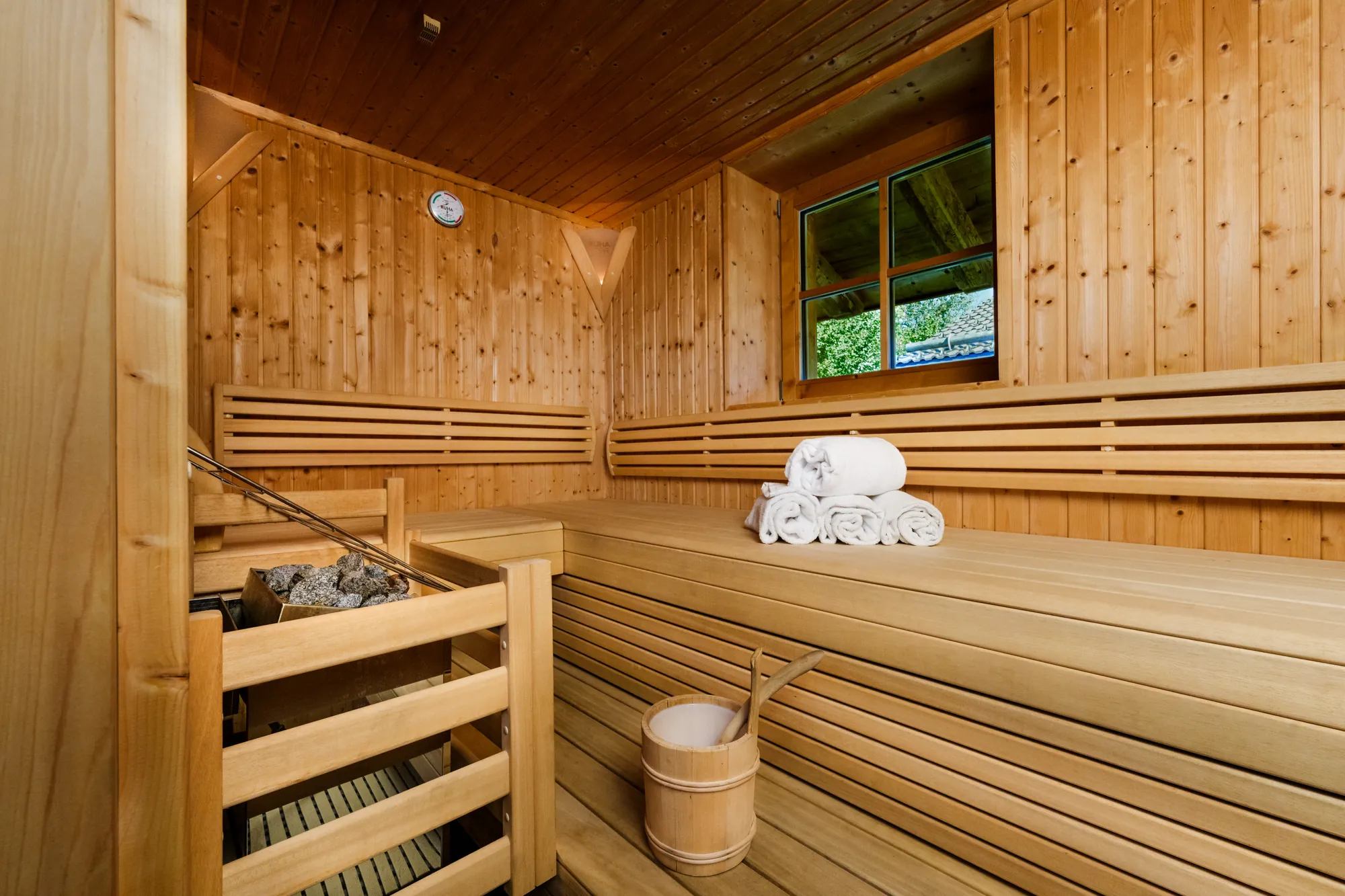 Finnish sauna in light wood with benches, sauna stove, towels, bucket and a small window