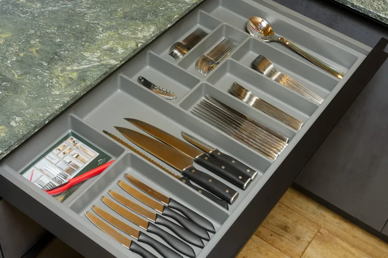 Cutlery drawer with knives, forks, spoons and several kitchen knives below the stone worktop