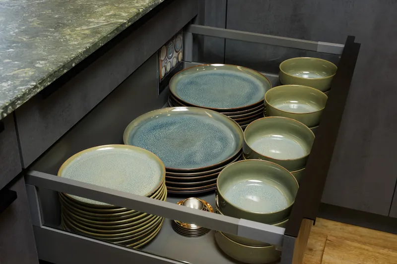Open kitchen drawer with stacked green ceramic plates and bowls