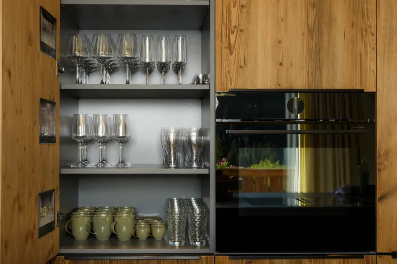 Open kitchen cabinet with wine and water glasses, mugs and a built-in oven in a wooden front