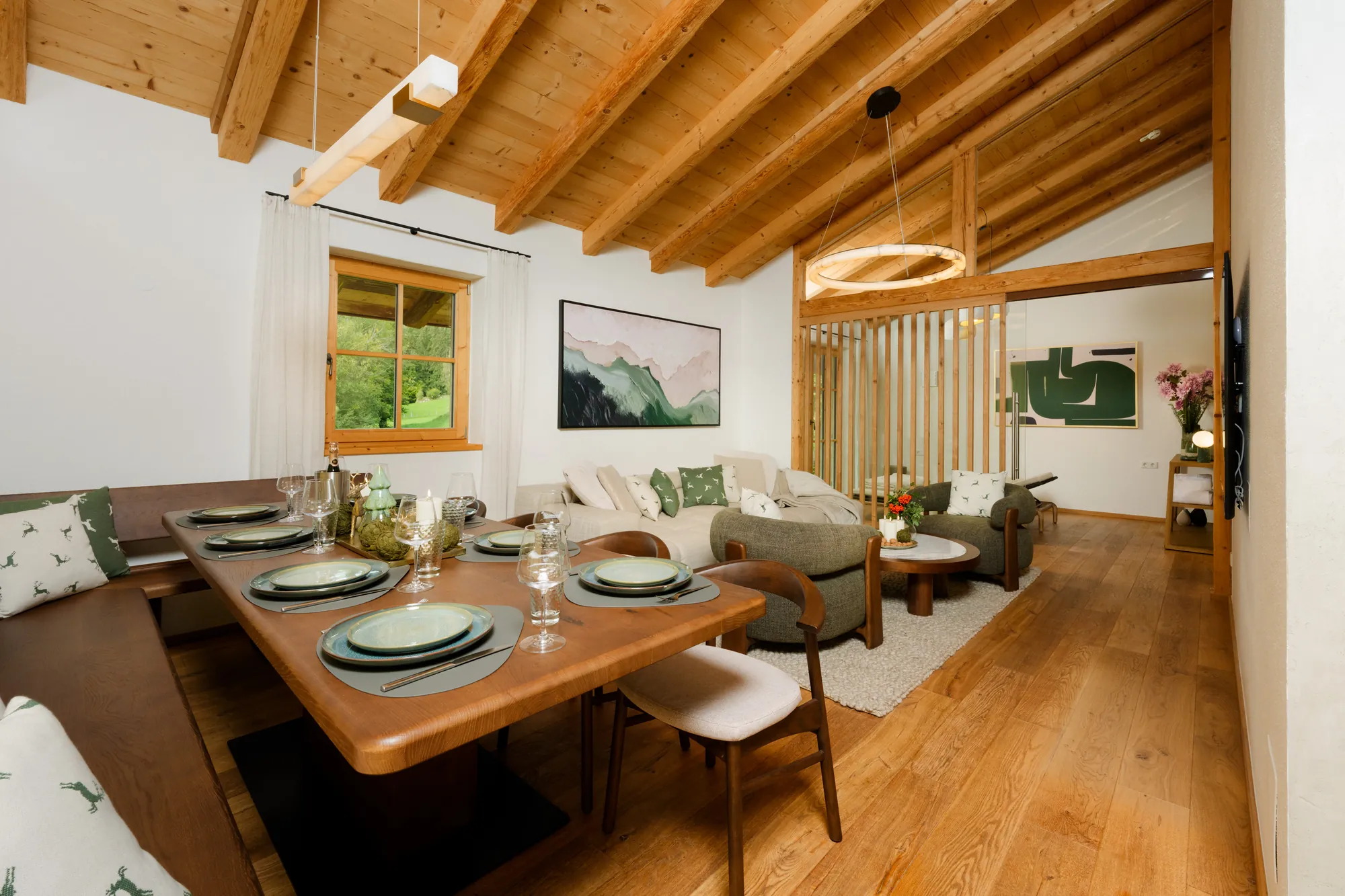 Open-plan living and dining area with a set wooden table, sofa, armchairs and exposed timber roof beams