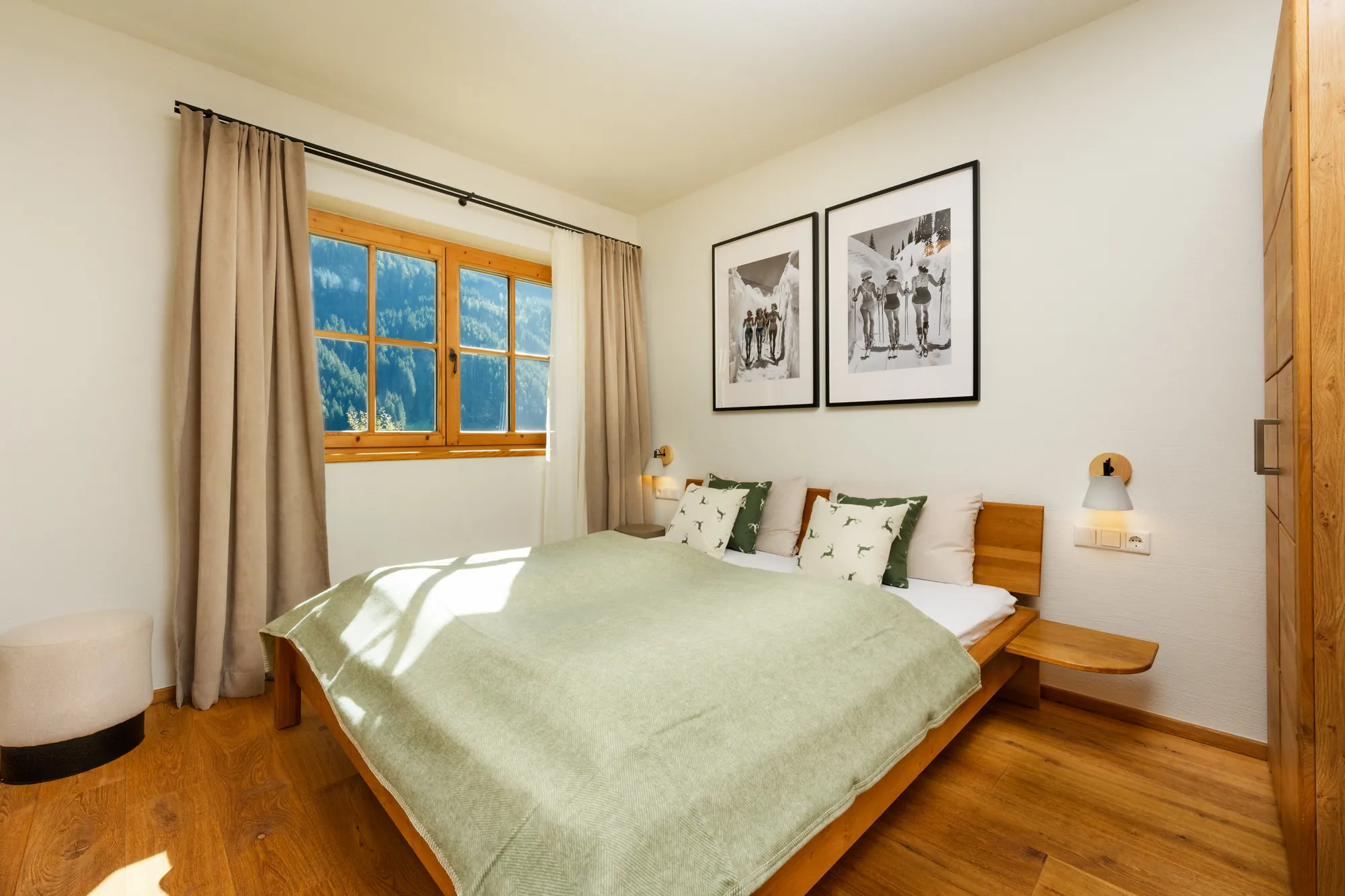 Bedroom with wooden king-size bed, green bedspread, deer cushions, black-and-white ski photos and a window with mountain view