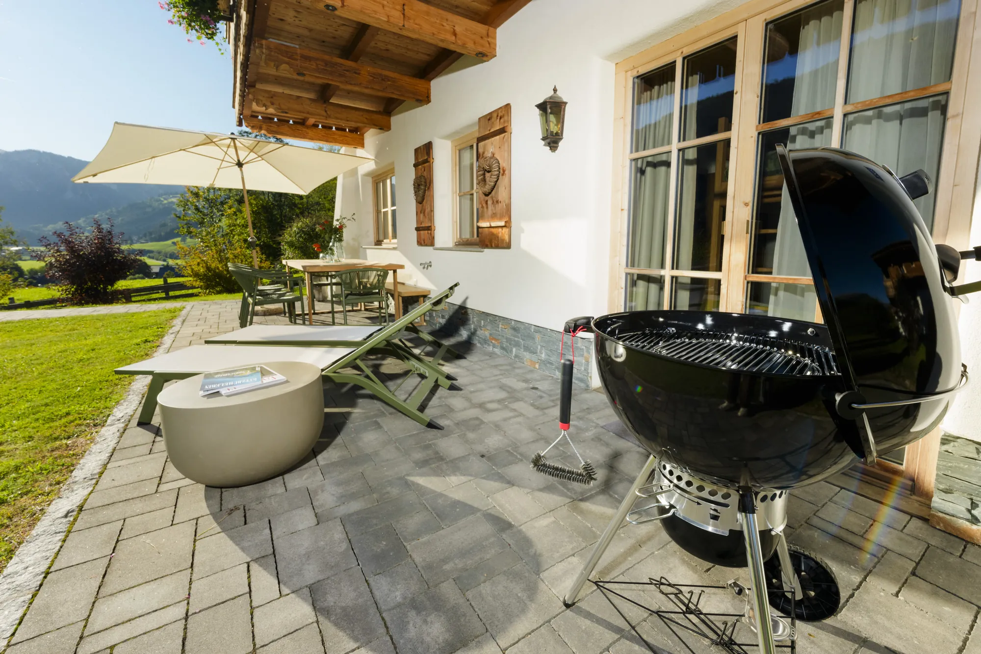 Terrace of Chalet Gams with black kettle barbecue, sun loungers, parasol and view of the garden