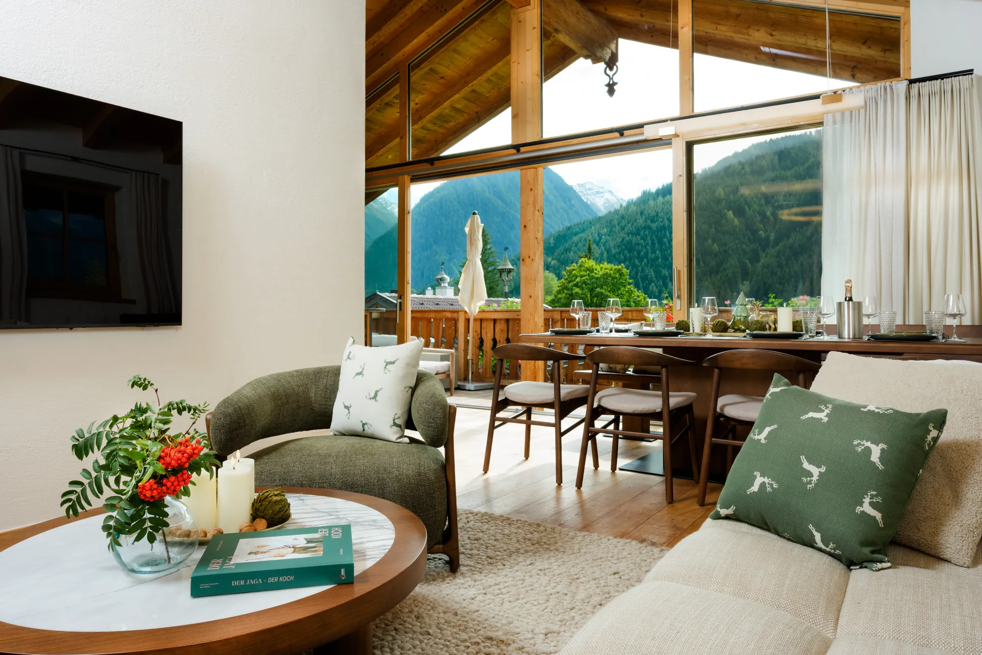 Armchair and coffee table in the living area, dining table and large glass front with balcony and mountain view behind