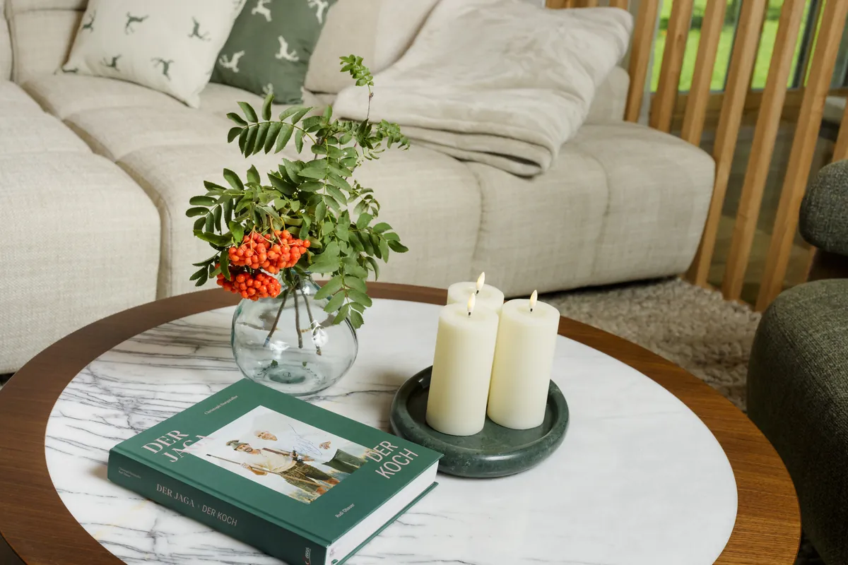 Round marble coffee table with candles, a vase with a rowan branch and a green book in front of a light sofa at Chalet Gams